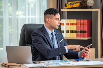 A man in a suit is sitting at his desk, looking at his phone.
