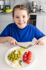 Happy little girl eating spinach waffles, celery and cherry tomatoes. Concept: delicious, healthy...