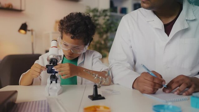 Curious boy and dad examine samples under microscope, conducting experiment