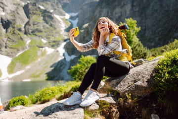 Tourist woman taking a selfie in nature on top of cliff with valley mountains view, sharing travel adventure journey. Lifestyle, travel, tourism, active life.