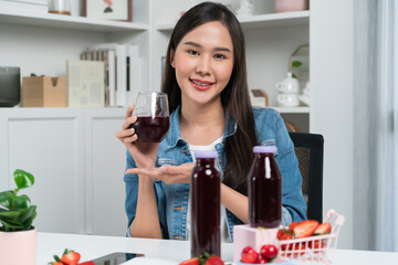 Smiling young beautiful Asian reviewing tasty mixed strawberry and cherry juice detox drinks,...