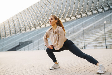 Fototapeta premium Smiling woman stretching her legs before jogging outdoors in the morning. Sport, gym and healthy body concept.