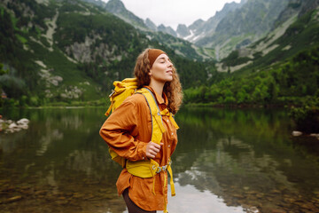 Woman traveler with yellow hiking backpack and hiking stiks enjoys the scenery. Active lifestyle....