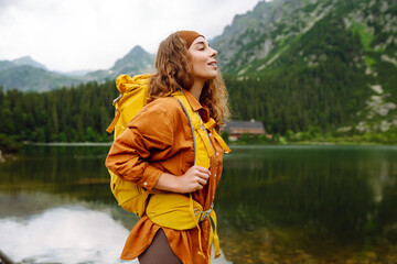 Woman traveler with yellow hiking backpack and hiking stiks enjoys the scenery. Active lifestyle. Wanderlust.