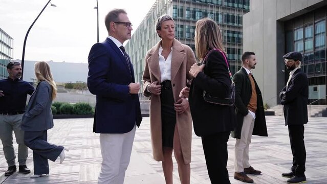 Group of business people gathering outside financial district discussing project ideas together after seminar. Zoom in footage.