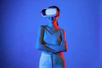 Smart female standing hit by neon light wearing VR headset connecting metaverse, futuristic...