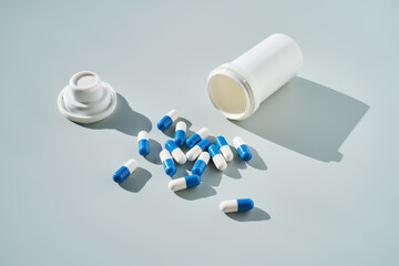 Blue and white capsules spilled out of a medicine jar on a blue background.