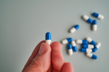 A hand holds a white and blue pill on a blue background.