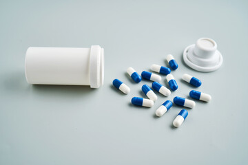 Blue and white capsules spilled out of a medicine jar on a blue background.