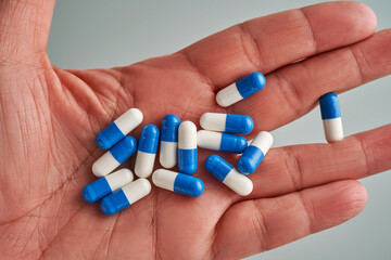 A hand holds a handful of white and blue pills on a blue background.