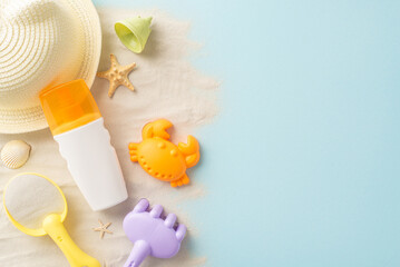 Beach safety for kids. Overhead shot of SPF lotion beside sand play set: rake, shovel, hat, sand and more. Vibrant pastel blue backdrop with space for text