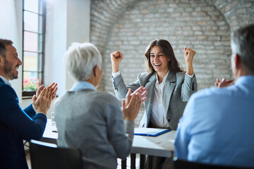 Cheerful woman celebrating getting a job on an interview with human resource team who is applauding...
