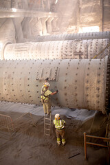 Workers are repairing the grinding mechanism in the workshop of a cement plant. Work technology,...