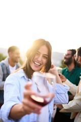 Vertical. Point of view of pretty young woman toasting with glass of red wine in hand smiling. Girl...