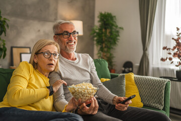 Mature senior husband and wife watch scary movie and hold popcorn