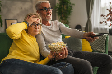 Mature senior husband and wife watch scary movie and hold popcorn