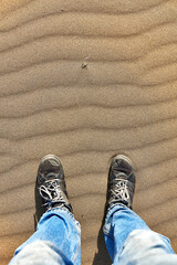 top view of mans legs standing on the surface of a sand dune