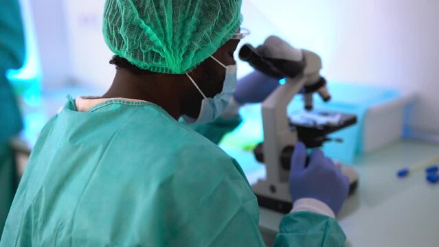 African male scentist using microscope while working inside laboratory - Virus research concept