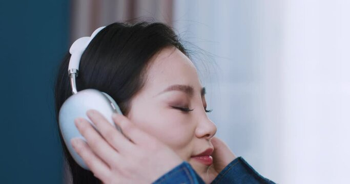 Side view of Asian young girl enjoying listening to music in her wireless headphones. Closing eyes while music playing by digital device. Moving her head to rhythm of melody. Wellbeing. Hobby concept.