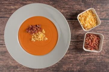 Plate of salmorejo accompanied by two bowls with its ingredients, egg and ham on a rustic table
