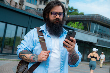 a bearded man looks at the phone on the street.