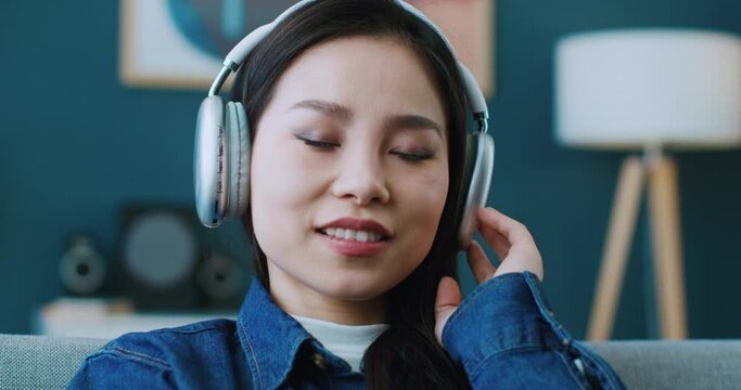 Portrait of Chinese woman using headphones while listening her favourite music. Enjoying new song. Spending free time with pleasure. Joyfully exclaiming and smiling when her best playlist starts.