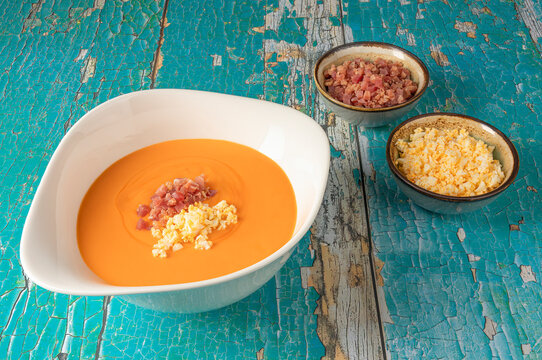 White bowl of salmorejo and its ingredients, bread, garlic, tomato, oil on an old table