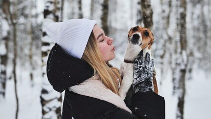 A girl cuddles a Jack Russell Terrier dog in the woods in winter.
