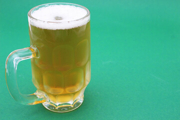 Image of a glass of beer with foam on a green background.