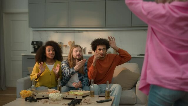 Multiracial friends multiethnic people buddies women men guys girls together at home gathering fun Caucasian woman standing front showing pantomime explaining object game teenagers trying guess word