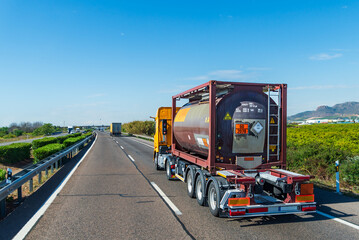 Truck driving on a highway with a tank container with labels and danger panels for toxic liquids...