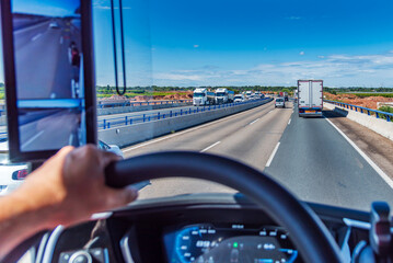View from the driving position of a truck of a three-lane highway crowded with vehicles. Dense traffic.