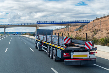 Truck loaded with iron beams, oversized load with its signaling panels of red and white stripes on...