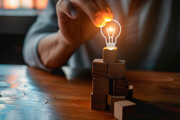 Wooden cubes with icons of head and light bulb on them, hand picking one cube from the top to make tower over wooden table background for ideas concept