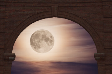 view of the full moon illuminating the clouds in the night sky through a brick arch