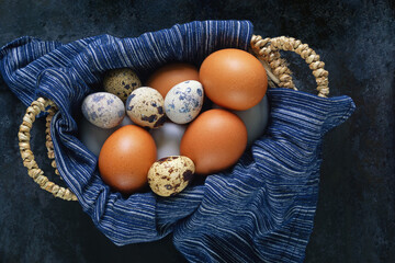 Chicken eggs and quail eggs in small basket on  black table