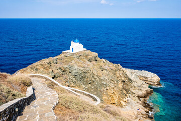 Coastal path with steps to small church built on rocks and blue sea in background in Kastro...