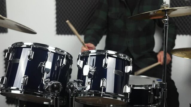 Close-up of an adult drummer playing a blue drum kit in a studio.