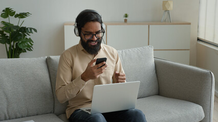 Arabian muslim man in headphones with laptop listen pop rap music enjoying musical audio track on...