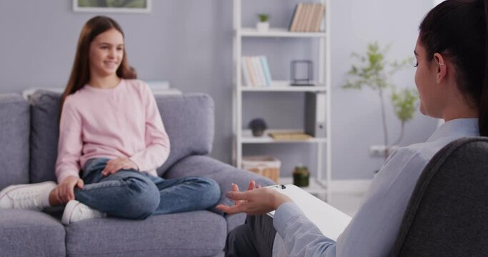 Portrait of a psychologist woman doctor making notes consulting teenage child girl smiling patient during therapy session at office. Psychotherapy and kids mental health concept. 4k video.