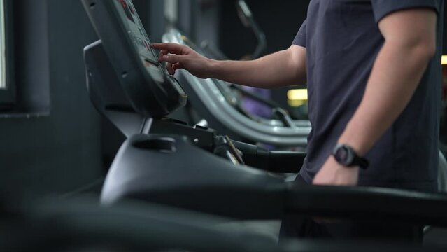 Cropped shot of unrecognizable athletic man walking on treadmill preforming warming-up run routine exercise in gym. Sporty male with fitness tracker walking on treadmill, working on health and fitness