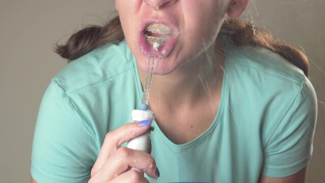 Young woman cleans braces with Water flosser, dental irrigator. Orthodontic oral hygiene.