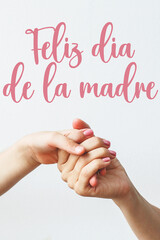 hand of child and mother on white background text happy mother's day in Spanish, sweet wishes...