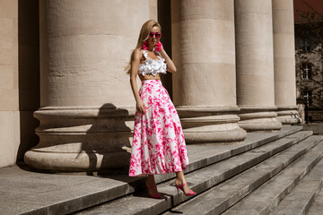 Elegant, stylish woman in pink floral dress and sexy high heels is sensually walking in the city on...