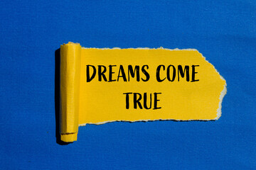Dreams come true words written on torn yellow paper with blue background. Conceptual dreams come...