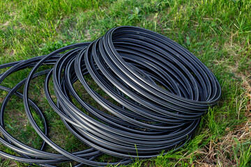 Black HDPE pipe for water supply, wound in a roll on the grass. Installation of water supply and...
