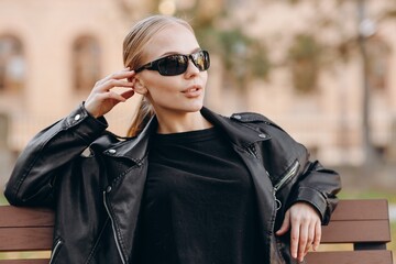 A confident girl with black sunglasses on her eyes, looks away is wearing a black t-shirt, leather...