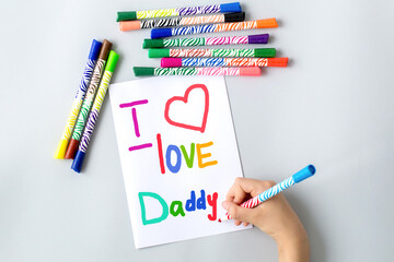 child draws with multi-colored felt-tip pens a poster gift card for dad for the holiday Father's...