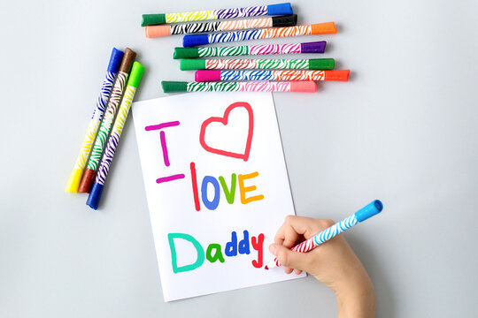 child draws with multi-colored felt-tip pens a poster gift card for dad for the holiday Father's Day with the text i love daddy and heart, sweet wish concept