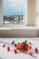 bowl of strawberries on a table next to a window. Home dining room interior. bowl with ripe...